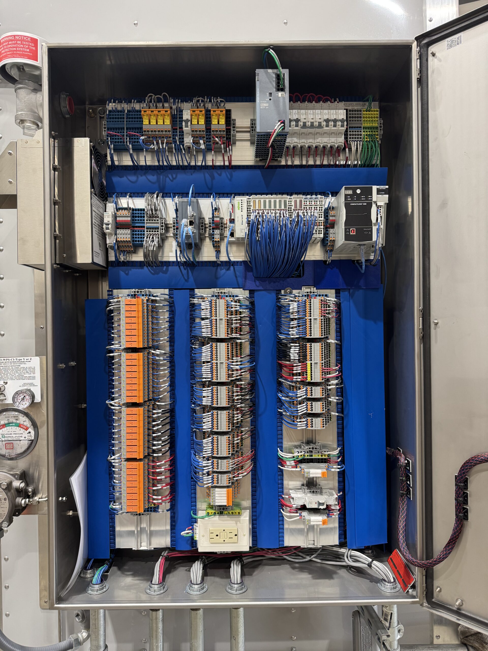 Interior of a Class 1 Division 2 control panel showing CompactLogix PLC, dense terminal block I/O section, relay banks, and remote I/O modules mounted on blue DIN rail backplates inside a stainless enclosure